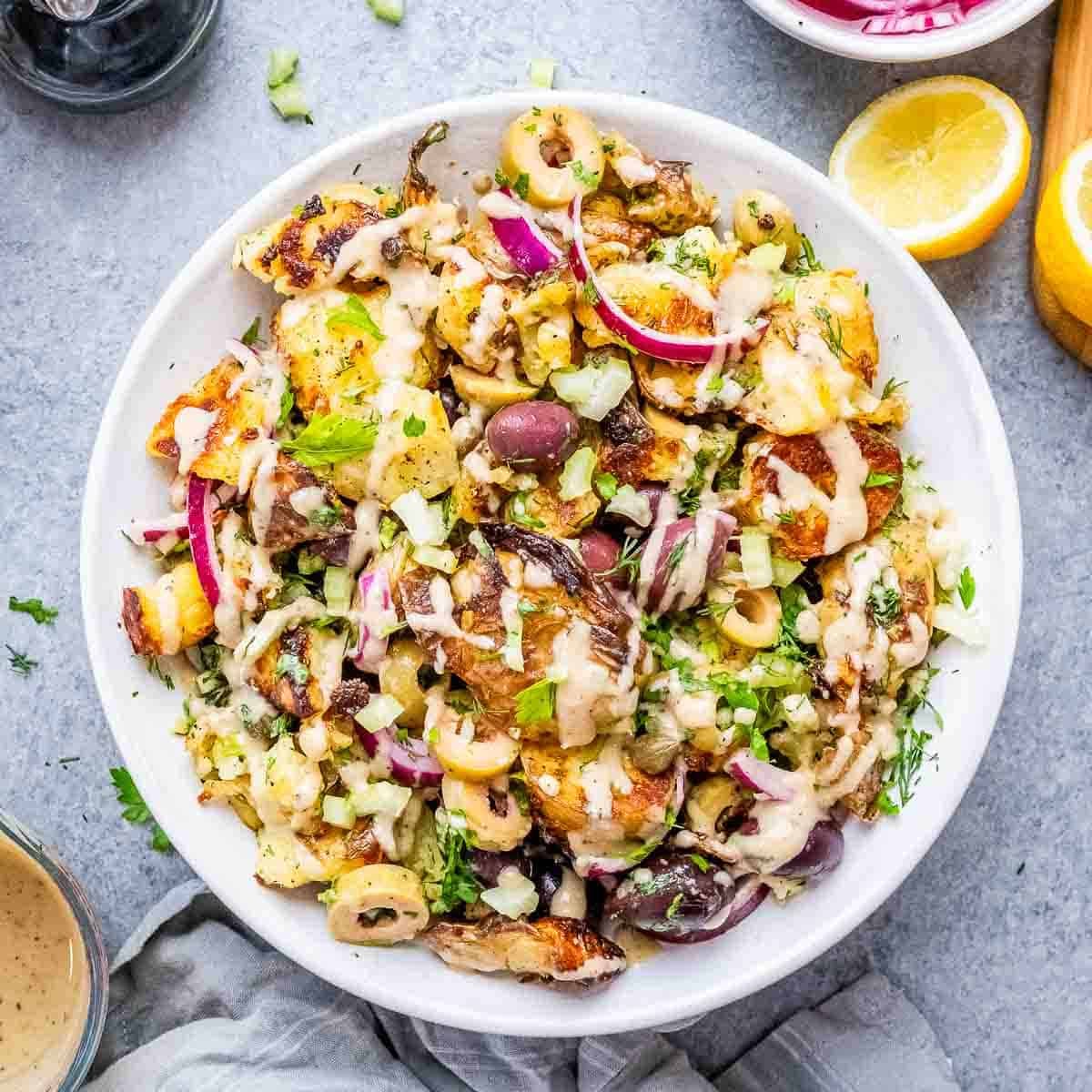 Batatas amassadas e douradas em uma tigela rústica, decoradas com ervas frescas e um fio de azeite sobre mesa clara