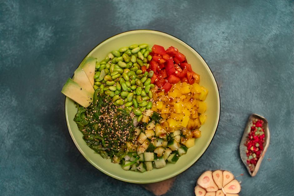 Tigela de salada verde com edamame, gengibre ralado, sementes de gergelim tostado e rodelas de limão sobre mesa de madeira