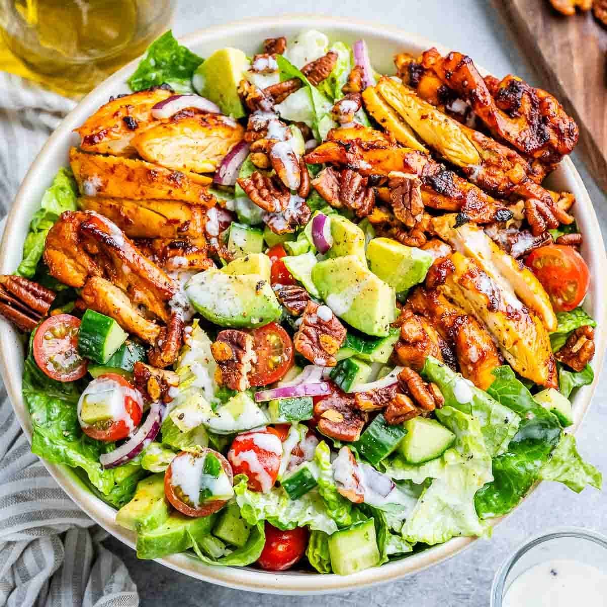 Tigela de salada colorida com peito de frango grelhado, molho BBQ e vegetais frescos sobre uma mesa de madeira