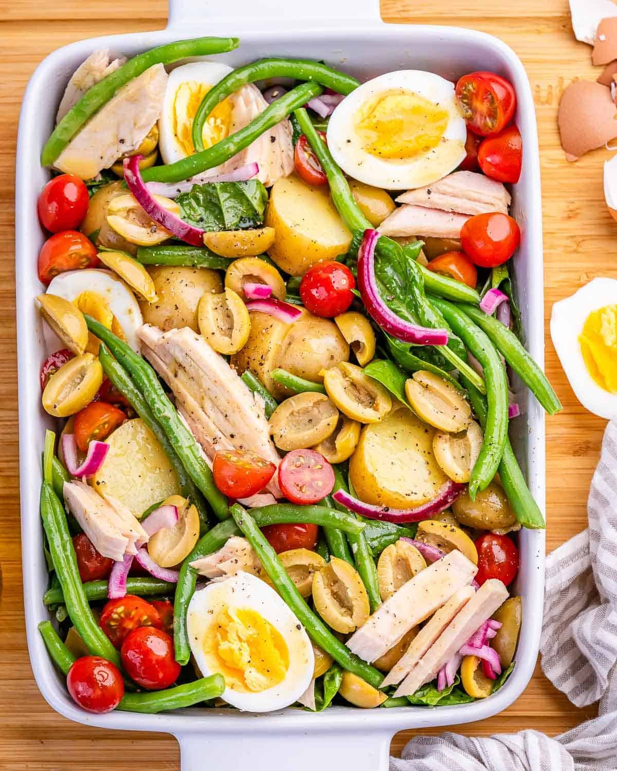 Prato de Salada Niçoise com atum, ovos cozidos, azeitonas, vagem e batatas sobre uma mesa rústica bem iluminada