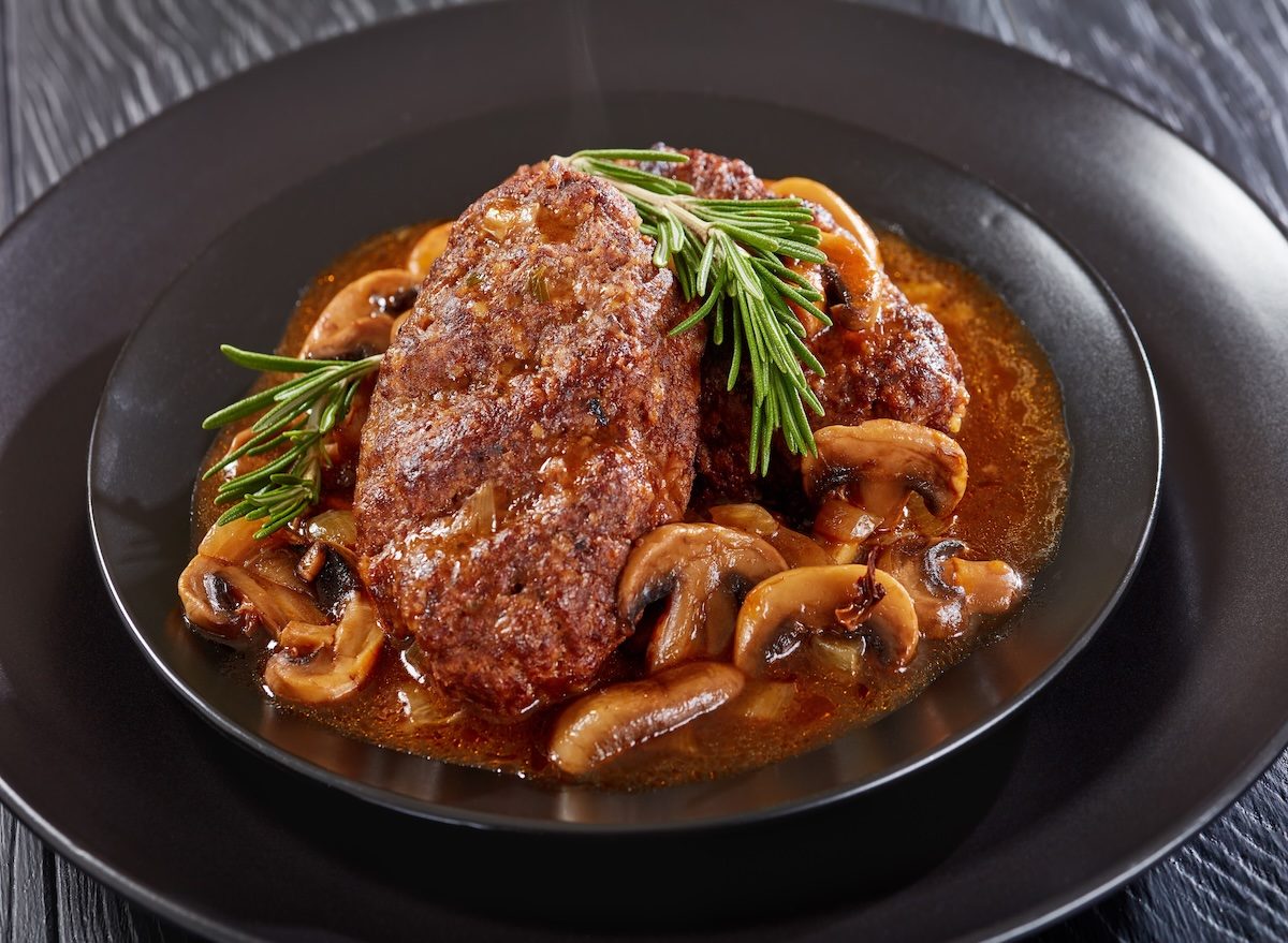 Prato de Salisbury steak com purê de batata, molho gravy e brócolis ao lado, acompanhado de garfo e copo d'água