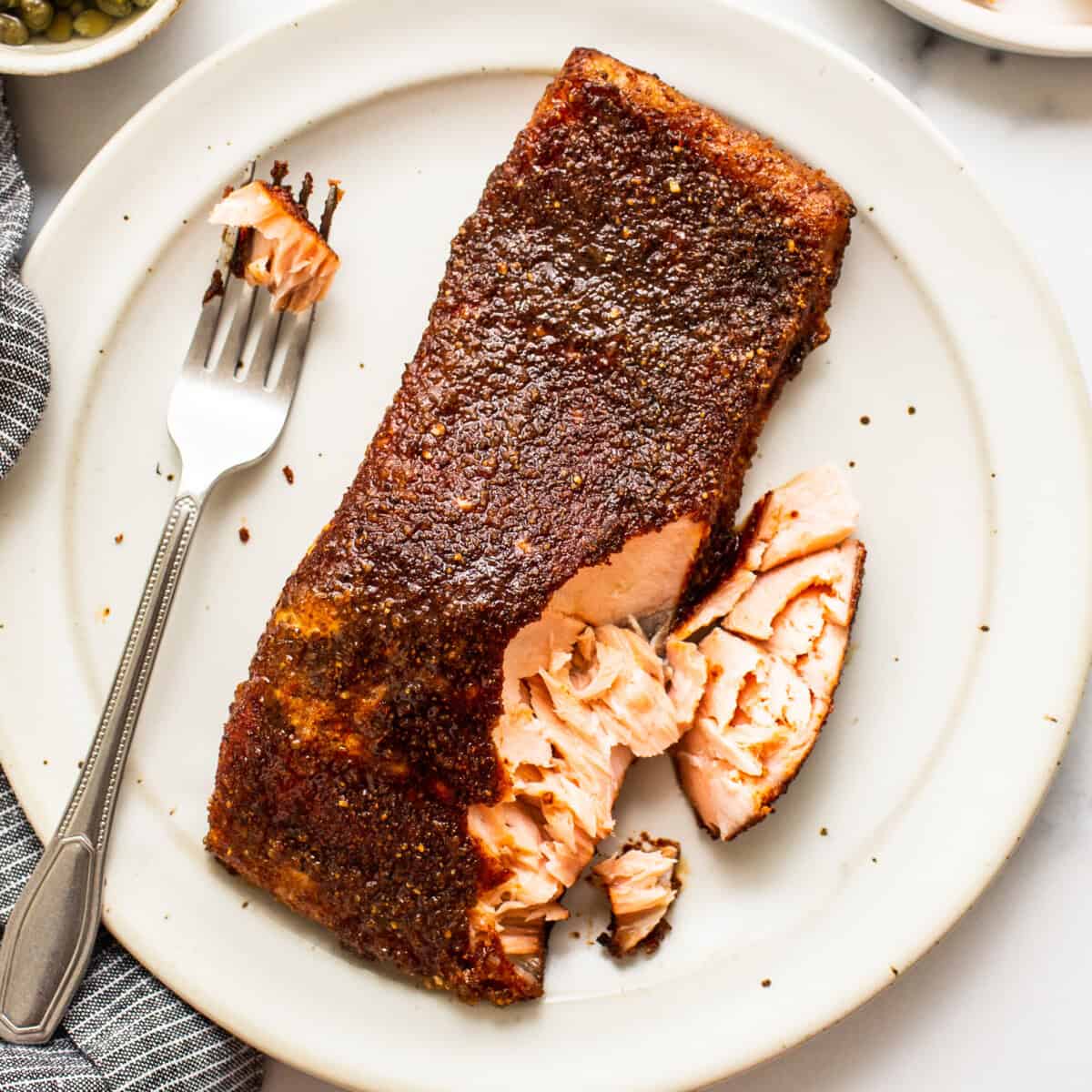 Pescador segurando um filete de salmão fresco, com uma frigideira ao lado, repleta de ingredientes para preparo saudável
