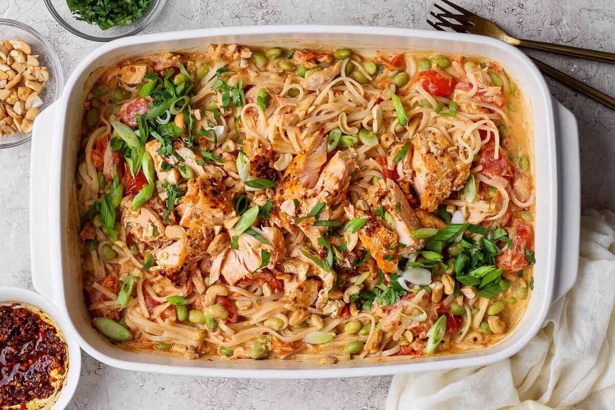Um prato de salmão fresco sobre noodles de arroz, coberto por molho cremoso e chili crunch