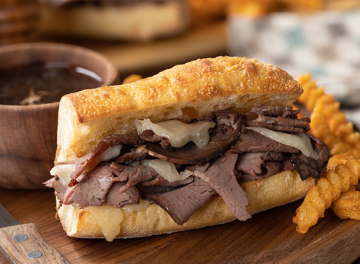 Sanduíche de carne assada suculenta em pão artesanal, acompanhado de molho au jus e uma salada verde fresca ao lado