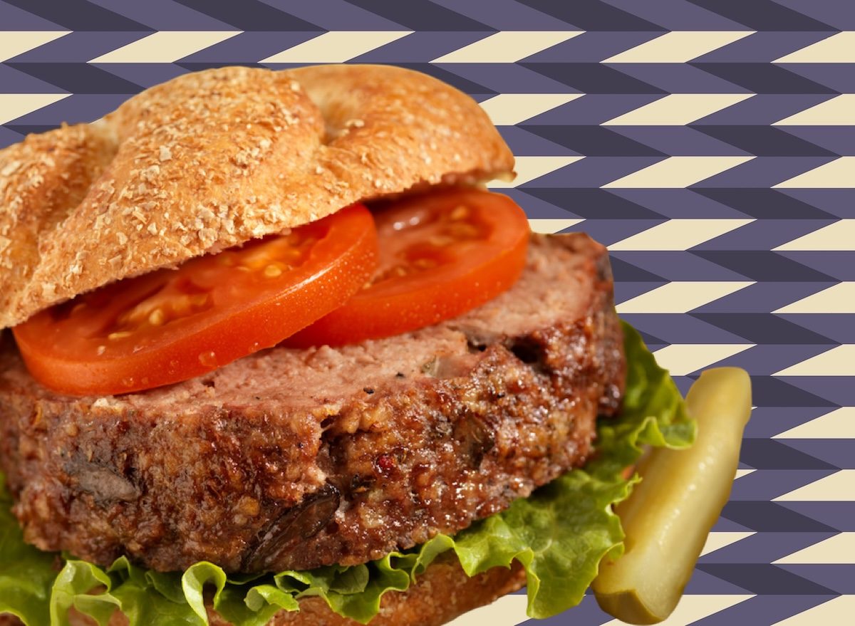 Fatias de carne moída grelhada entre pão integral, alface, tomate e molho de iogurte, sobre tábua de madeira