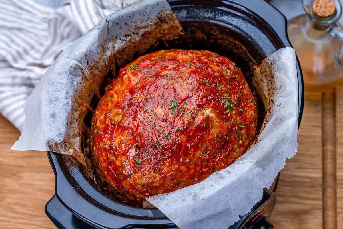 Carne moída de peru dourada no fundo da slow cooker, cercada por cenoura, cebola e um pincel de glaze de ketchup