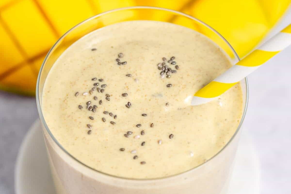 Manga congelada, iogurte grego, leite de amêndoas e sementes de chia ao lado de um copo de smoothie cremoso
