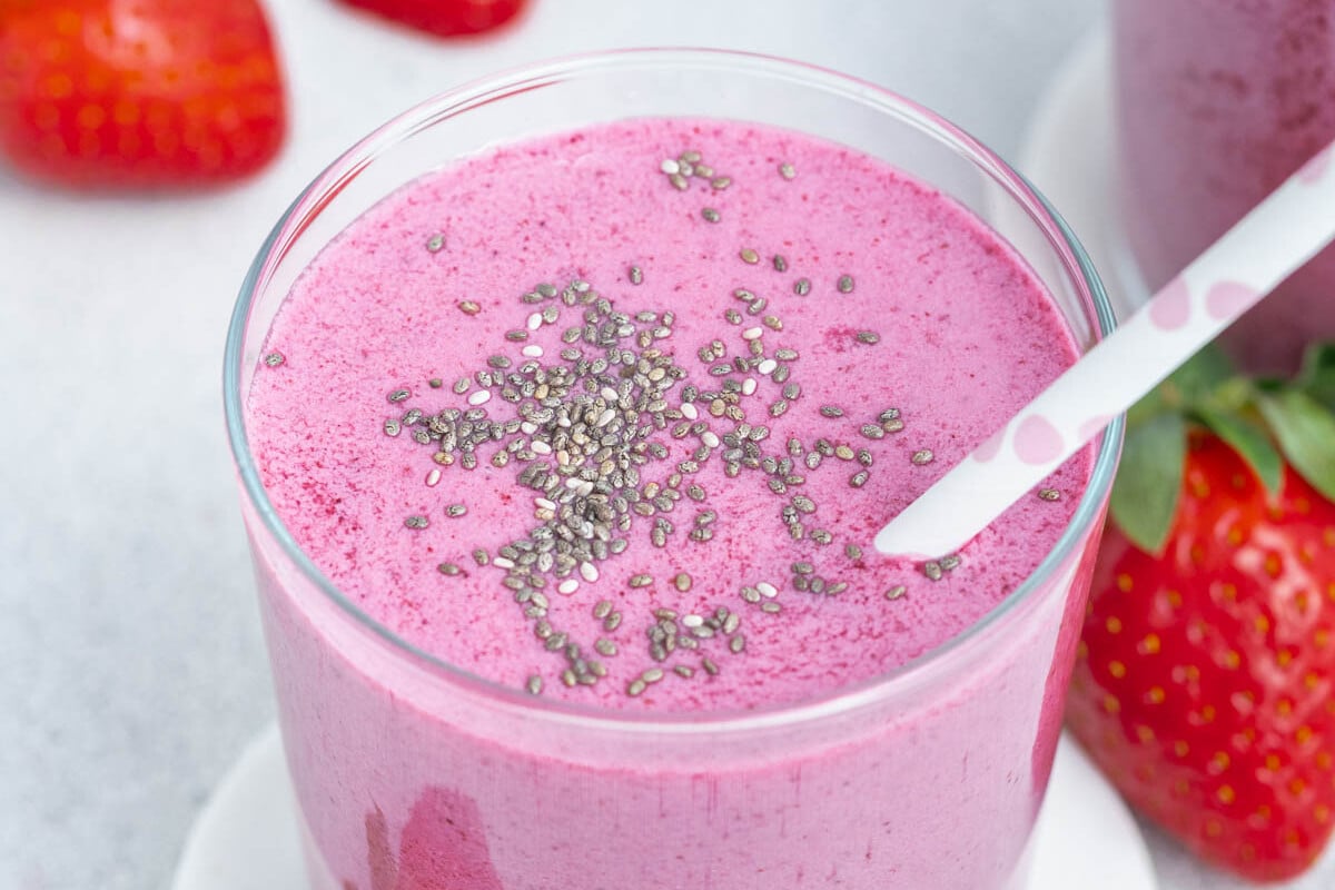 Smoothie cremoso de morangos e mirtilos em copo de vidro, ao lado de iogurte grego e frutas frescas sobre uma mesa