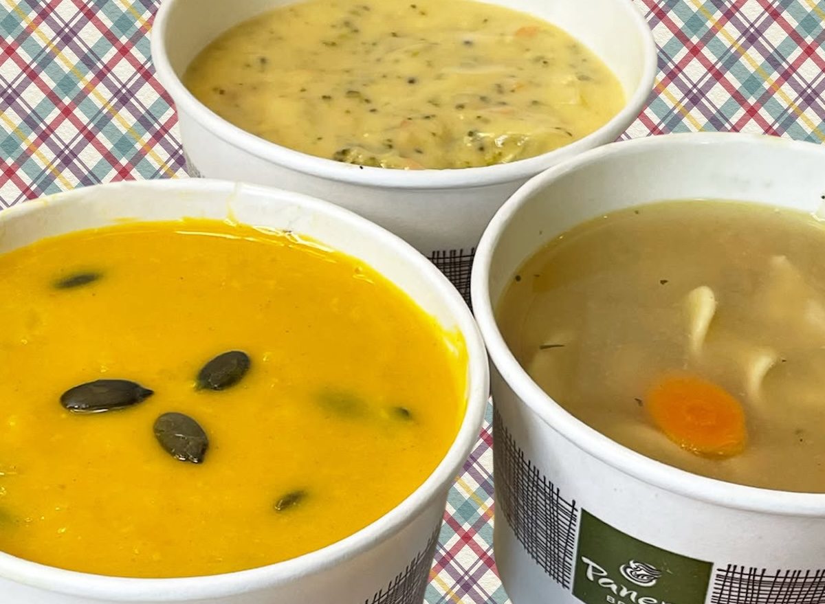 Tigela de sopa caseira com cenoura, brócolis, frango desfiado e temperos frescos sobre mesa de madeira