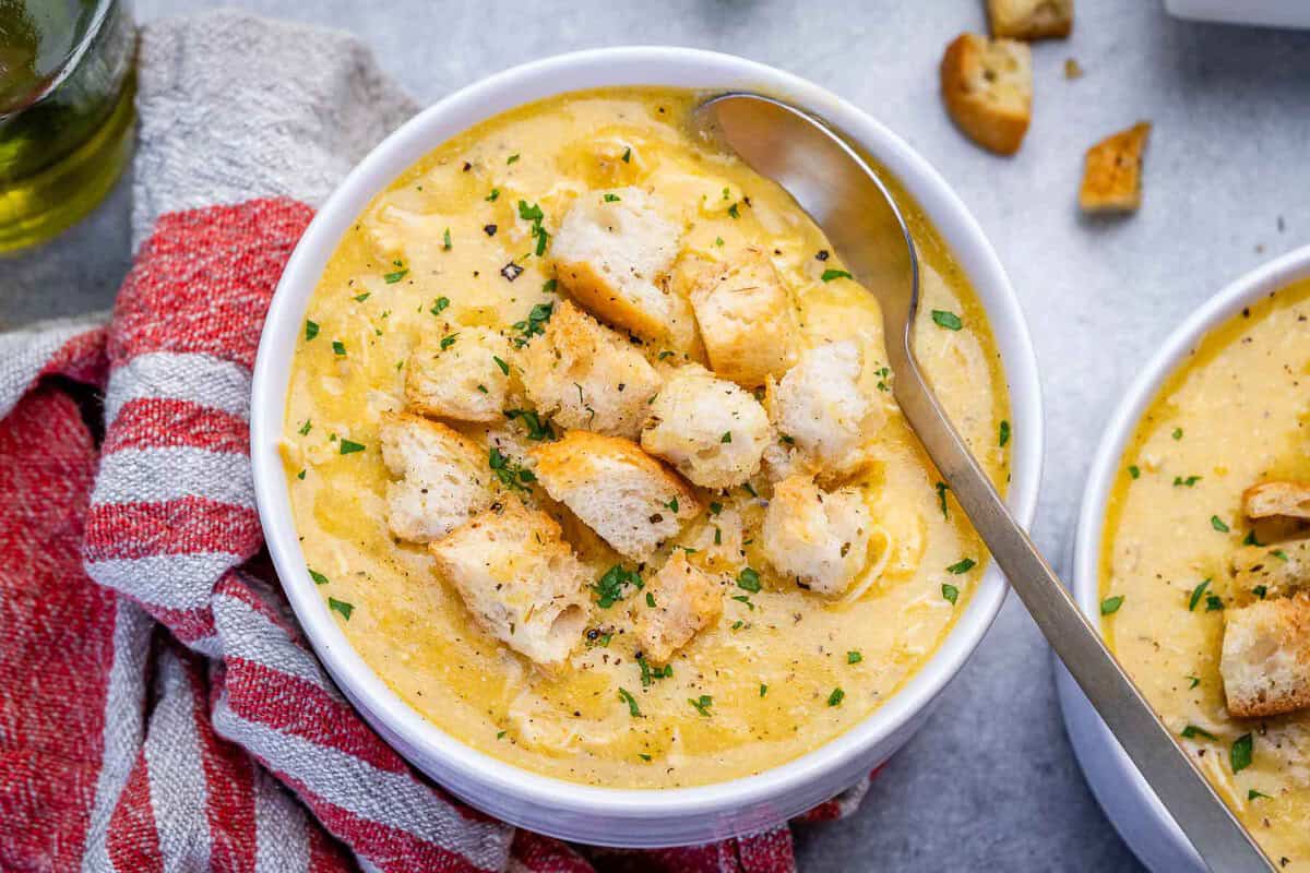 Um prato de sopa de frango caseira com vegetais picados e fatias de pão de centeio à mesa
