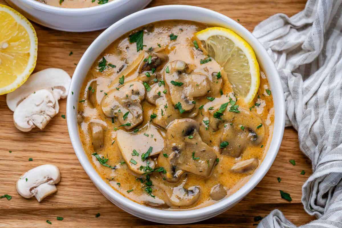 Tigela de sopa cremosa de cogumelos com iogurte grego, polvilhada com páprica e endro, ao lado de uma colher de madeira