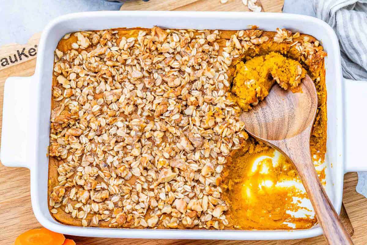 Soufflé de cenoura dourado em forma de ramequim, com cobertura crocante de nozes e aveia ao lado de cenouras raladas