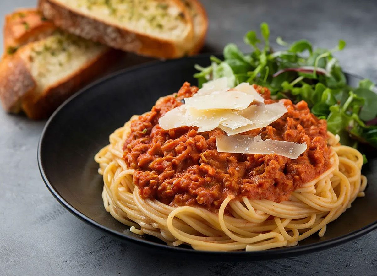 Spaghetti al dente ao lado de fatias douradas de pão de alho, garrafa de água e halteres sobre bancada de cozinha