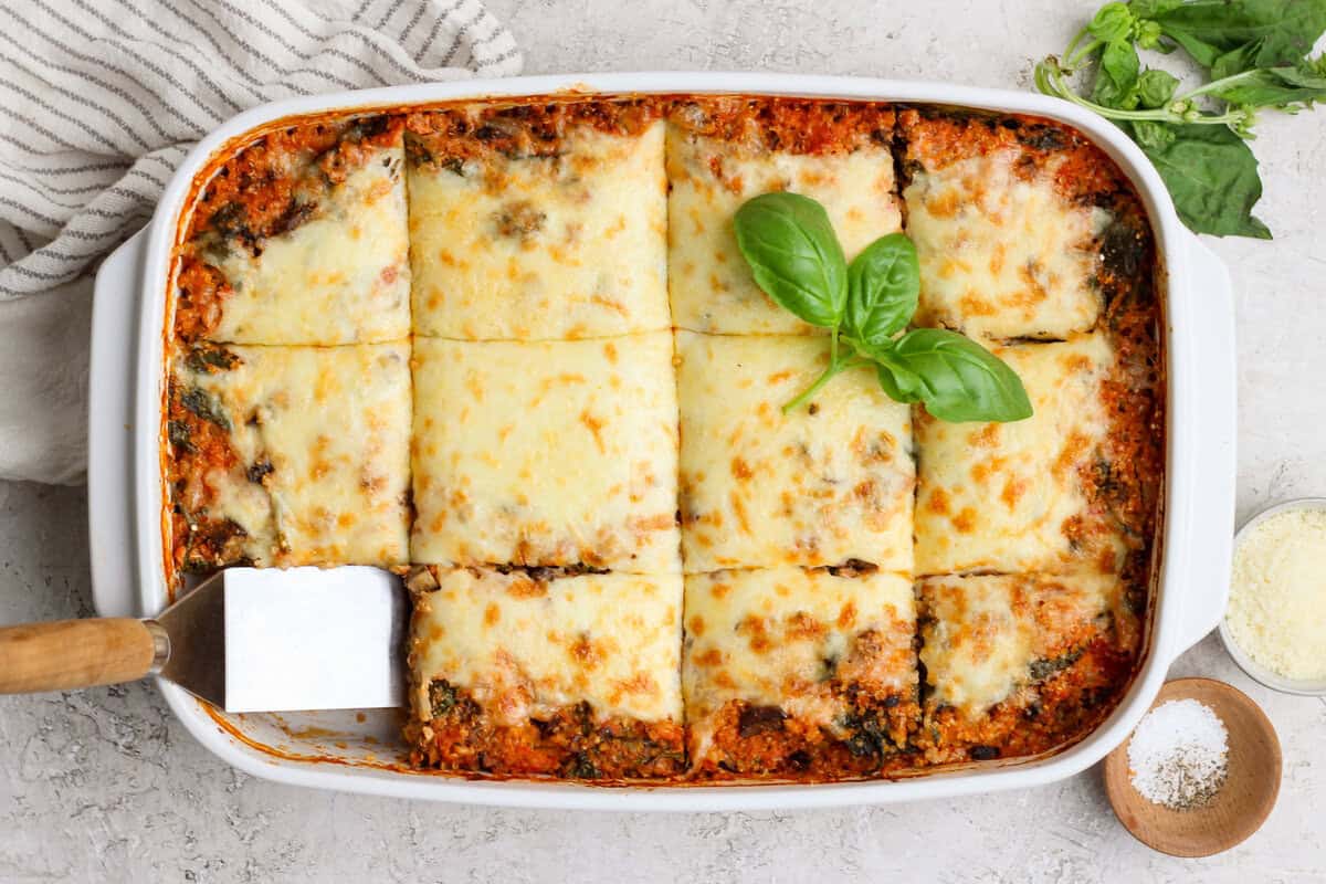 Lasanha vegana de quinoa e espinafre recém-assada, com camadas verdes de folhas, crosta dourada e garfo ao lado