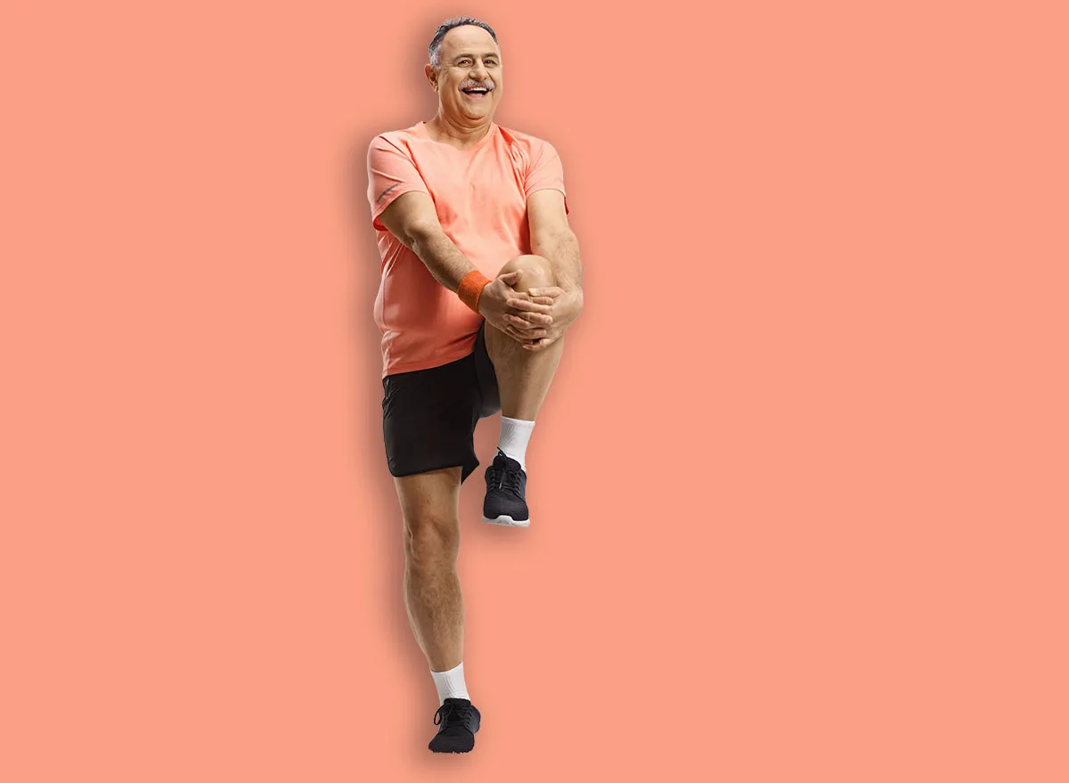 Uma mulher sorridente, com 60 anos, fazendo uma flexão de braço com pernas afastadas, mostrando força e mobilidade