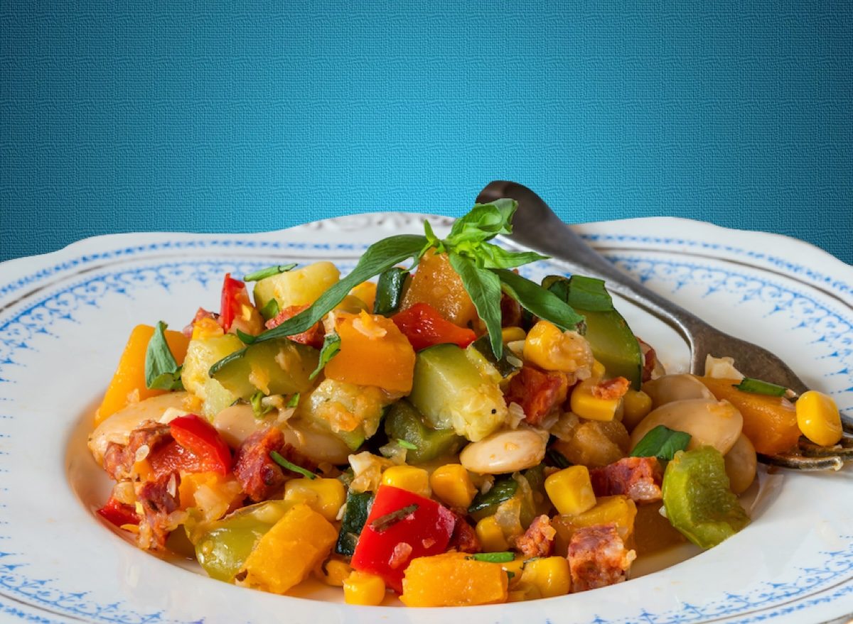 Prato colorido de succotash com milho amarelo, feijão verde, pimentão vermelho e abobrinha, ao lado de garrafa d'água