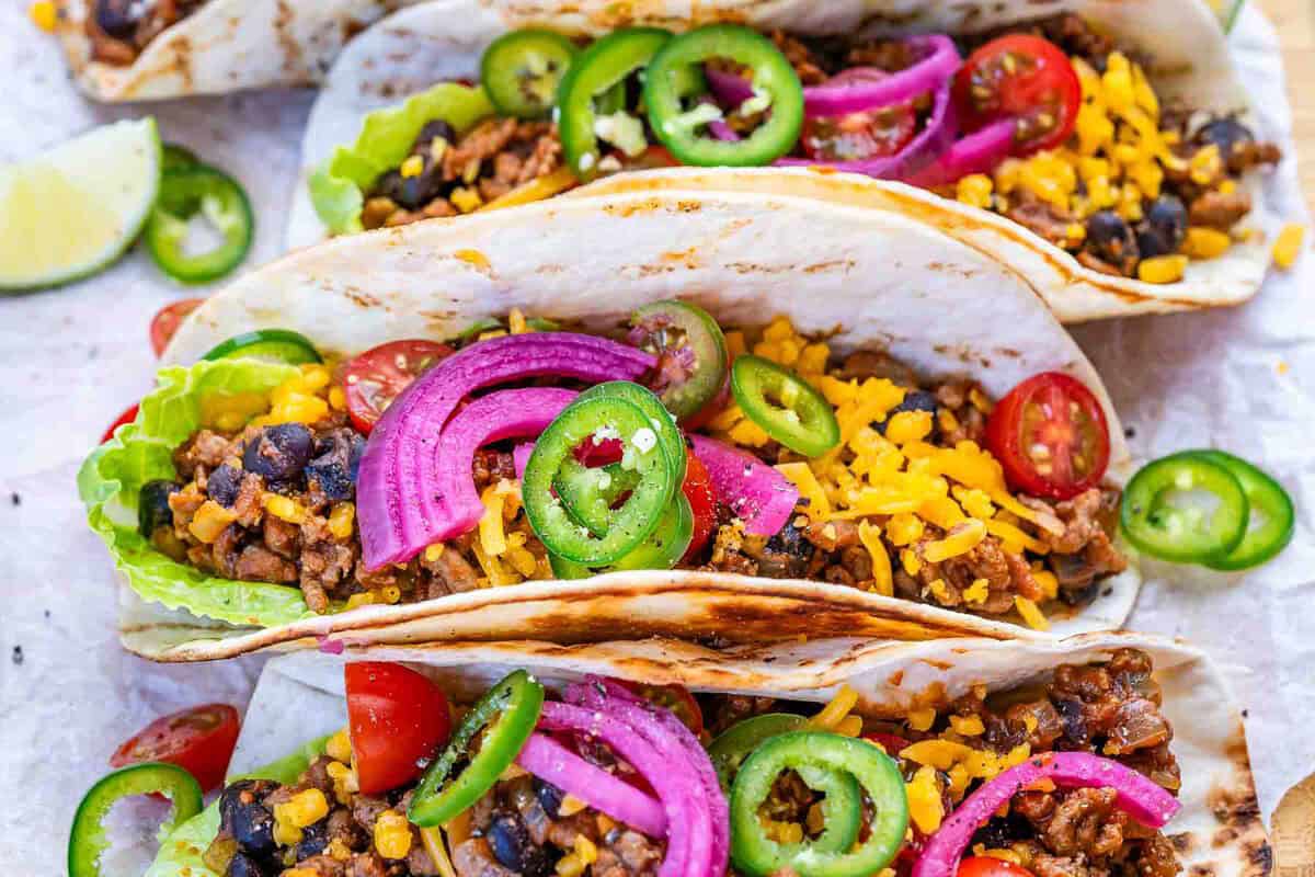 Tacos de carne moída com feijão preto dispostos em prato rústico, acompanhados de abacate fatiado e limão fresco