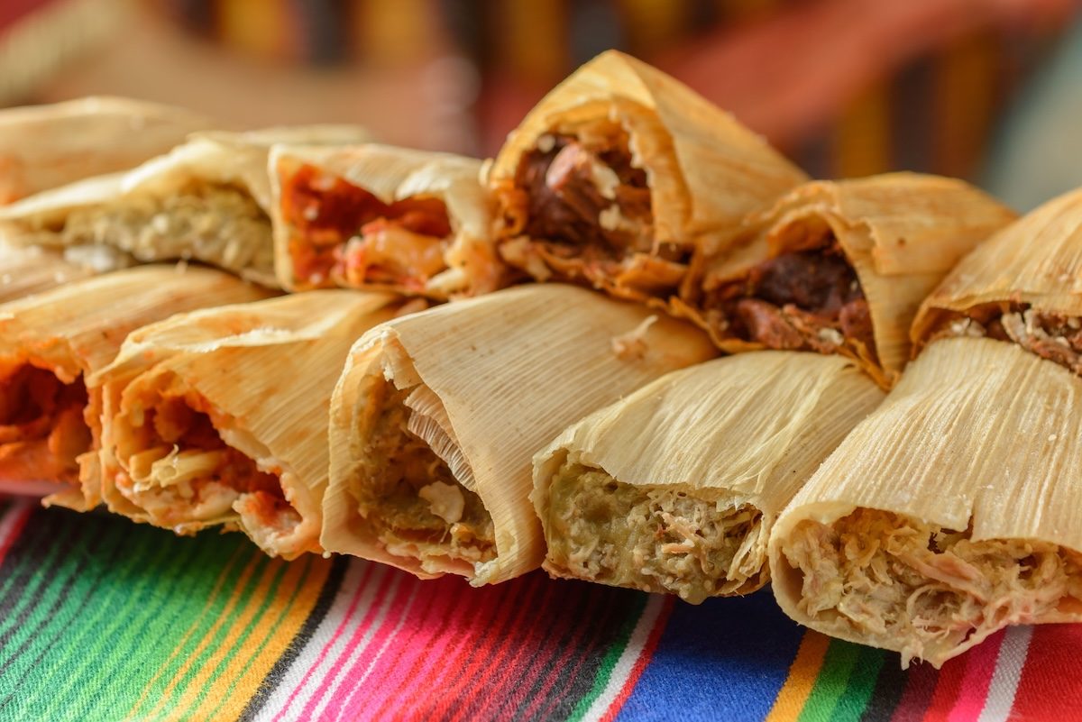 Tamales de milho ao vapor ao lado de uma tigela de guacamole, folhas de alface e um copo de água