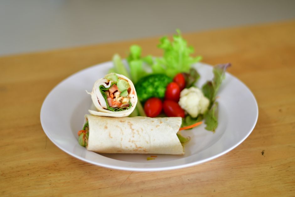 Tofu fatiado sobre pita integral, rodeado de alface, tomate, cenoura ralada e molho cremoso, pronto para enrolar