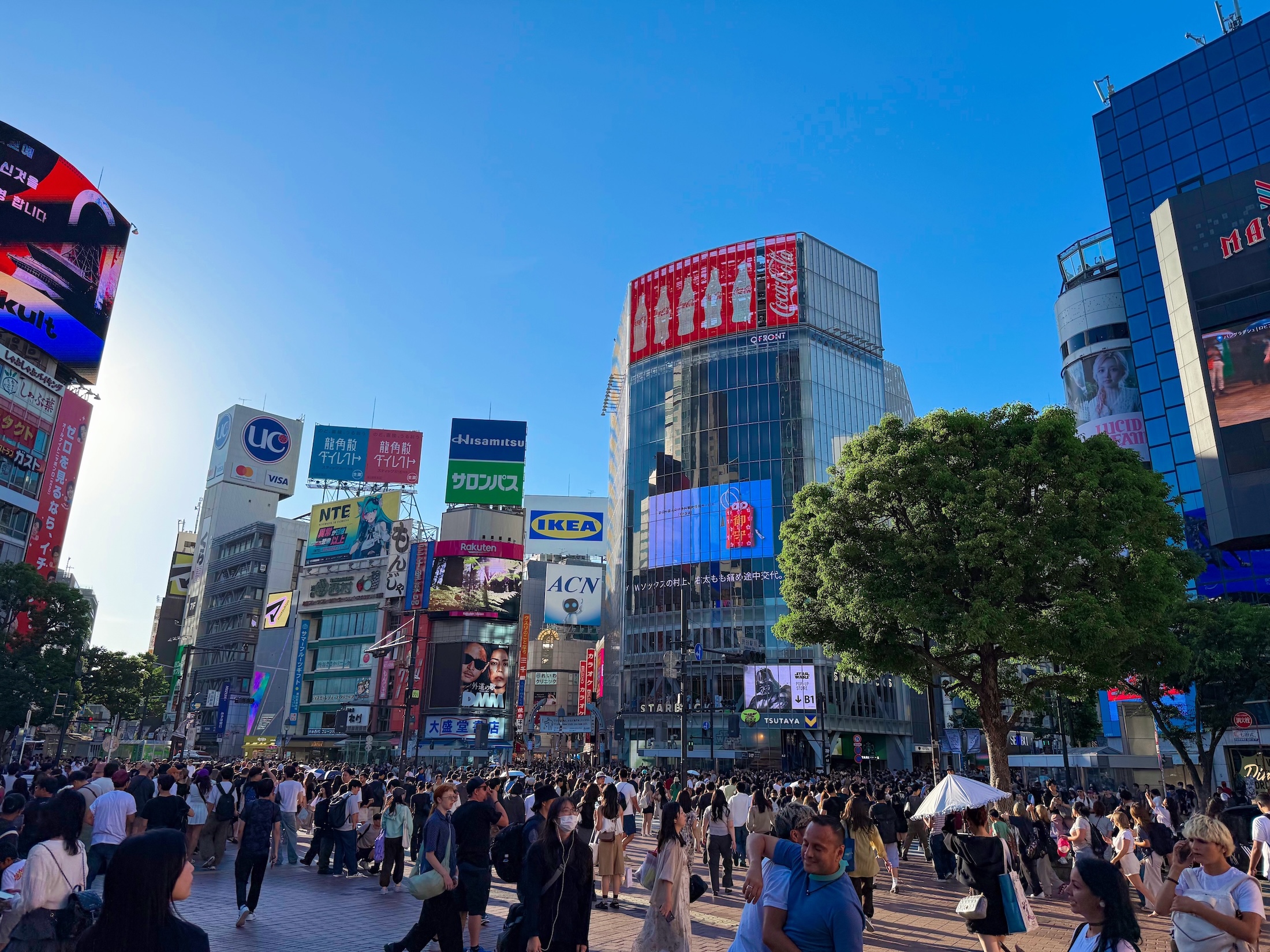 Jovem correndo na calçada de Shibuya, segurando garrafa d'água e passando por uma loja de konbini com onigiri