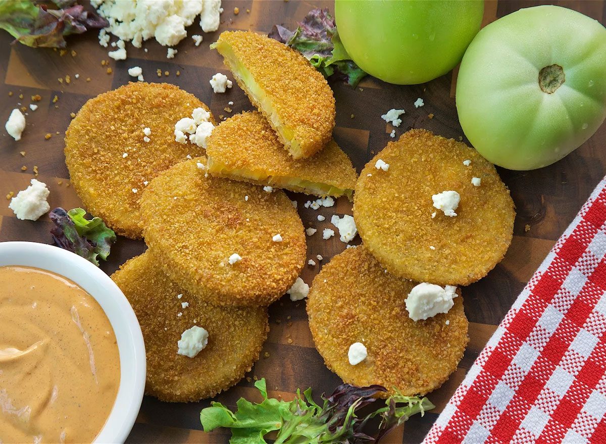 Um tomate frito verde crocante, com casca dourada e polpa firme, servido em uma tigela com folhas de manjericão frescas