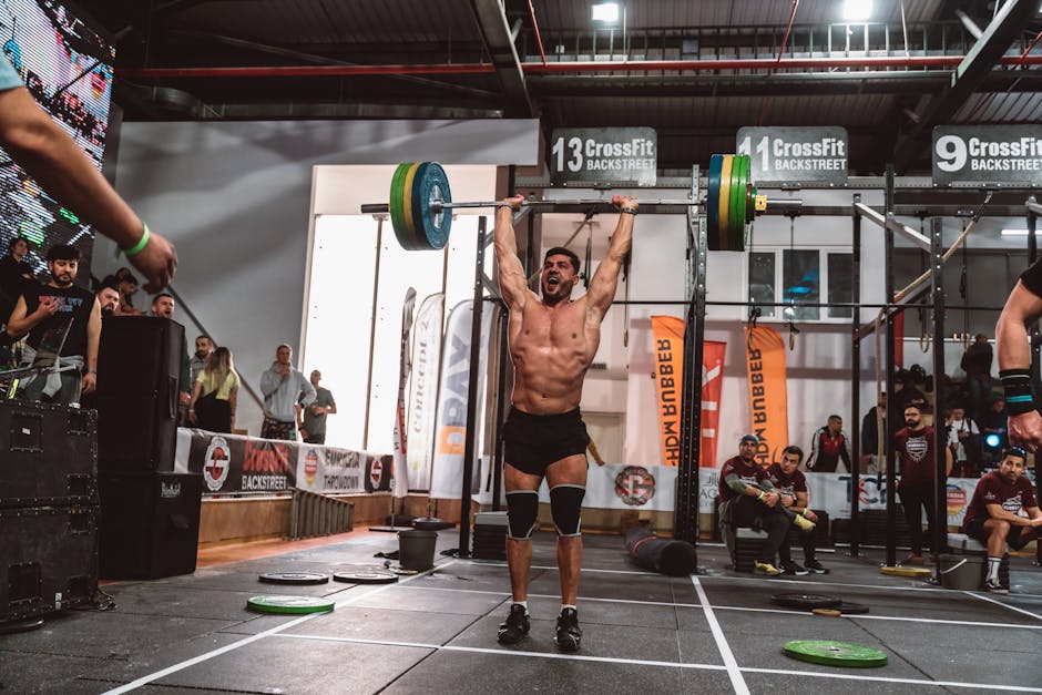 Atletas de CrossFit em esforço intenso durante um levantamento de peso olímpico sob luzes de arena profissional