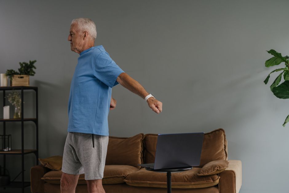 Uma mulher sentada em uma cadeira robusta, com uma faixa de resistência ao redor de seu corpo, apoiada na parede para equilíbrio