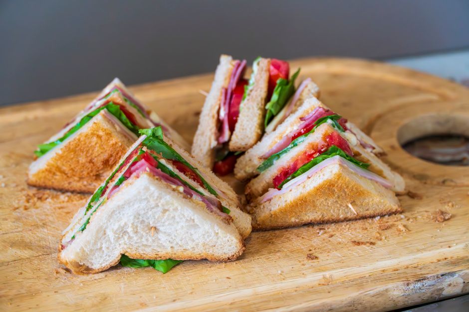 Pão integral empilhado com peito de peru, bacon crocante, alface, tomate e fatias de abacate, ao lado de maçã