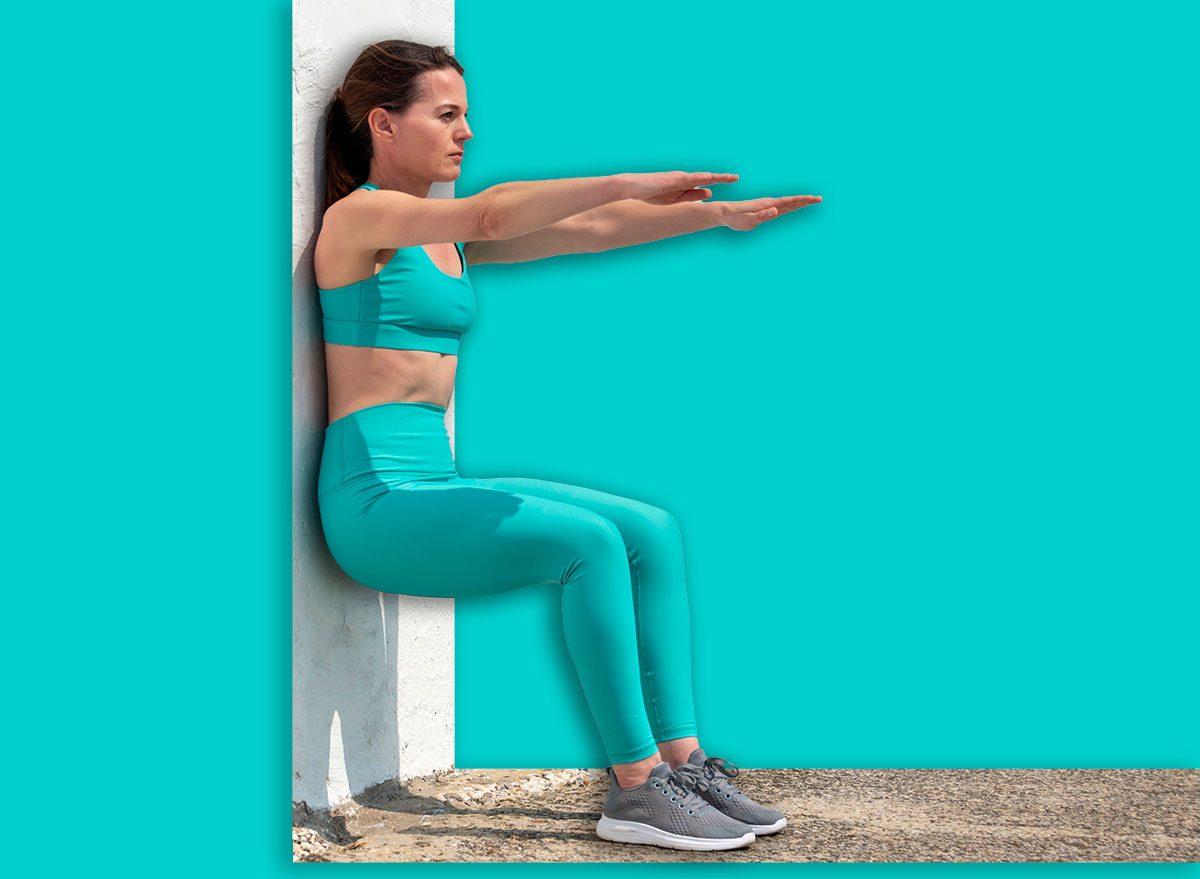 Pessoa de 70 anos fazendo wall sit, segurando halteres leves, ao lado de uma garrafa de água e um prato com peito de frango grelhado