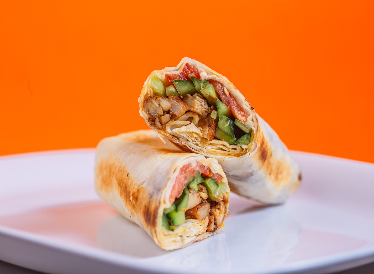 Wrap de frango com vegetais frescos fatiado ao meio sobre uma tábua de madeira ao lado de uma garrafa de água